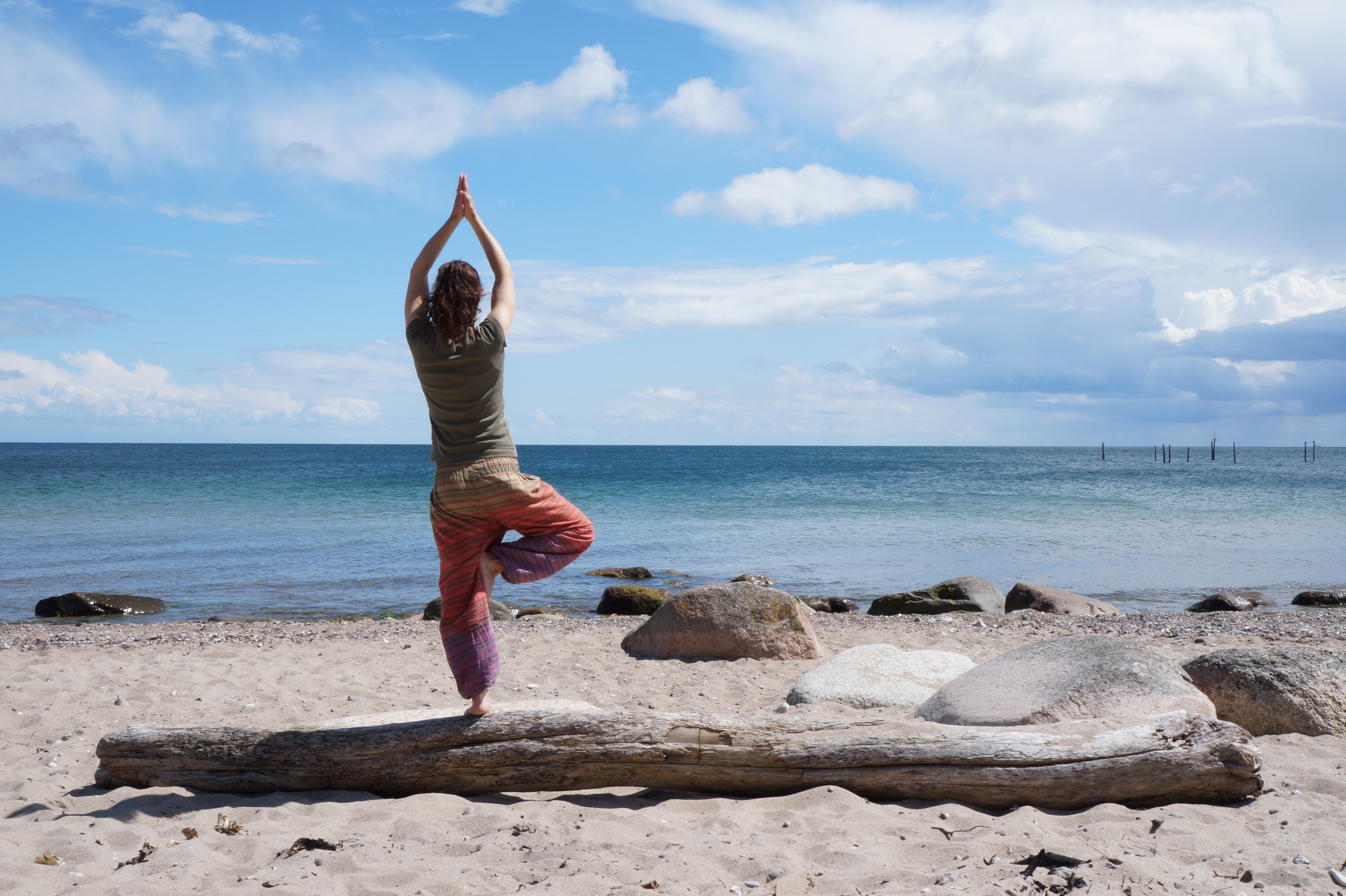 Rania Dimtsia von hinten am Strand, die eine Yogapose ausübt. Rania gibt Eltern-Kind-Yoga-Kurse in Köln.